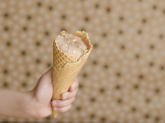 Chocolate ice cream in kid’ Hand on the beige background with space to the right