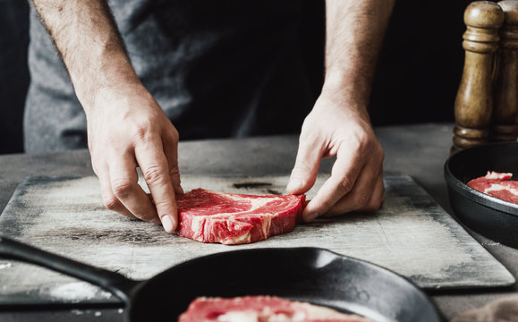 Man preparing beef steak on wooden table