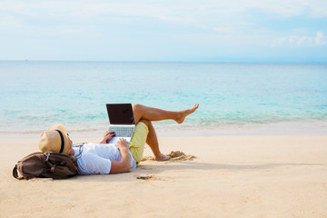 Man working on laptop computer while relaxing on the beach