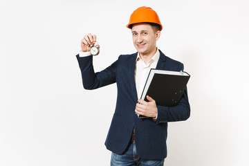 Young smiling businessman in dark suit, protective hardhat holding black folder for papers document and alarm clock isolated on white background. Time is running out. Male worker for advertisement.
