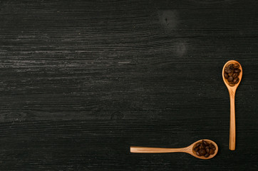 Coffee beans in wooden spoons and coffee scattered on a black table surface background with copy space. Top view.