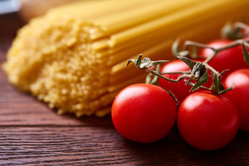 Uncooked pasta, tomatoes on wooden background, top view, close-up, selective focus