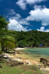 Tropical landscape of rocky beach with turquoise clean water and pier in the distance and blue sky. Saracen Bay, Koh Rong Samloem. Cambodia, Asia.