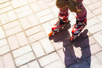 A little girl rolls on red rollers on the sidewalk. Shadow on the road. Active rest concept