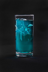 One-color, blue, transparent cocktail with ice cubes. Isolated black background. Side view. Drink in a glass glass for the menu restaurant, bar, cafe