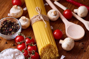 Uncooked pasta, tomatoes on wooden background, top view, close-up, selective focus