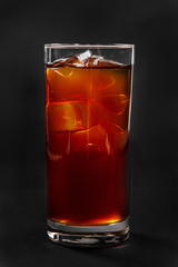 One-color, red, brown, transparent cocktail with ice cubes. Isolated black background. Side view. Drink in a glass glass for the menu restaurant, bar, cafe