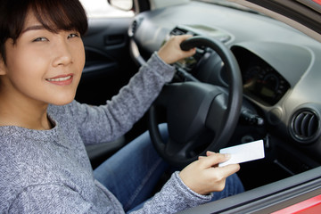 Obraz na płótnie Canvas Attractive young asian woman proudly showing her drivers license. Smiling woman holding her driver license after successful driver's exam in her red car.