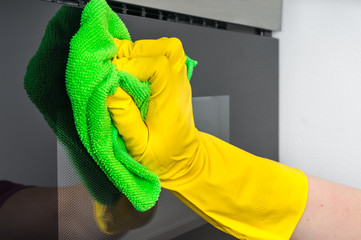 Hand in glove with green rag wiping microwave oven