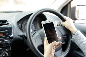 Woman holding mobile phone sending a text while driving a car. Selective focus.