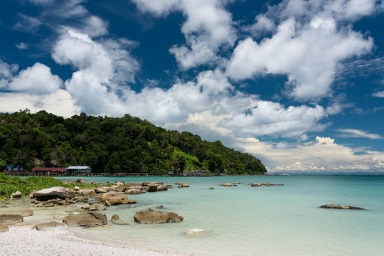 Tropical landscape of rocky beach with turquoise clean water and pier in the distance and blue sky. Saracen Bay, Koh Rong Samloem. Cambodia, Asia.