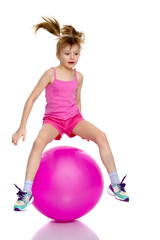 A little girl is jumping on the big gym ball.