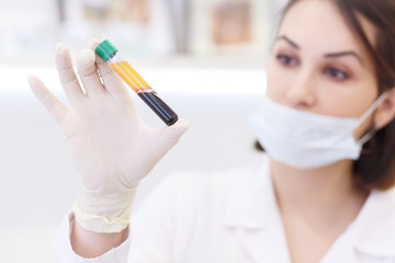 the young attractive doctor with mask on face in scrub and gloves holds in hand test tube with the...