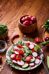 Creative fresh vegetable salad with ruccola, cucumber, tomatoes and raddish on white plate, selective focus