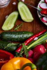 Fresh red radish in wooden bowl among plates with vegetables, herbs and spicies, top view, selective focus.