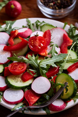 Creative fresh vegetable salad with ruccola, cucumber, tomatoes and raddish on white plate, selective focus