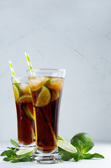 Fresh cold summer drink of cola, ice, lime, leaf mint on soft light white background, copy space.