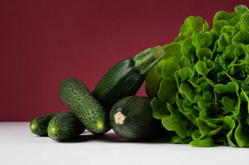 Dark colorful green vegetables on white table and bordo wall. Summer fashion food background.