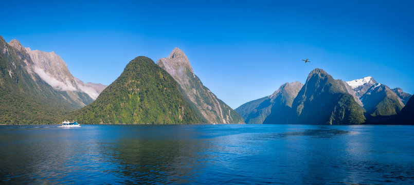 A small boat in the morning at Freshwater Basin in Milford Sound with Mitre Peak and numerous other Mountain Cliffs in Fiordland National Park, New Zealand, South Island.