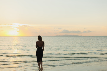Fototapeta premium rear view of woman standing in ocean during sunset