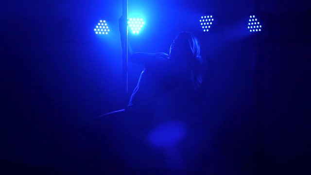 Silhouette of a sexy girl who does a complex exercise on a pylon in the dark. Slow motion.