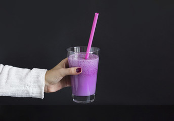 Female hand holds glass of berry smoothie with straw on black background. Pink milkshake with copy space. Healthy drink. Blueberry cocktail.