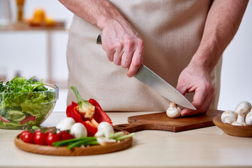 Man cooking at kitchen making healthy vegetable salad, close-up, selective focus.