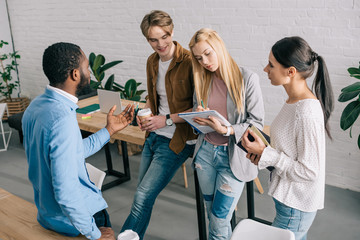multiethnic businesspeople with coffee and textbooks having discussion in modern office
