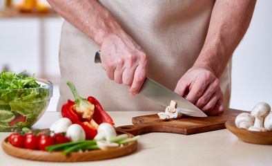 Man cooking at kitchen making healthy vegetable salad, close-up, selective focus.