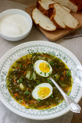 Vegetarian sorrel soup with egg, served with sour cream and bread. Rustic style.