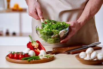 Man cooking at kitchen making healthy vegetable salad, close-up, selective focus.