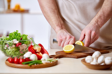 Man cooking at kitchen making healthy vegetable salad, close-up, selective focus.