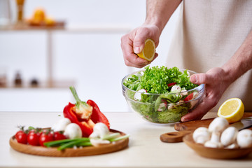 Man cooking at kitchen making healthy vegetable salad, close-up, selective focus.