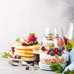 Oatmeal granola with berries and yogurt and panccakes on light gray concrete background. Healthy breakfast food concept with copy space.