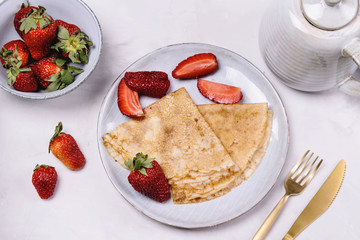 Openwork thin cheese crepes served with strawberry on grey concrete background. Homemade pancakes. Delicious breakfast
