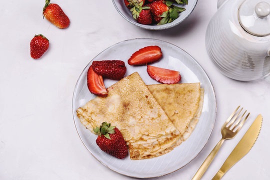 Openwork thin cheese crepes served with strawberry on grey concrete background. Homemade pancakes. Delicious breakfast