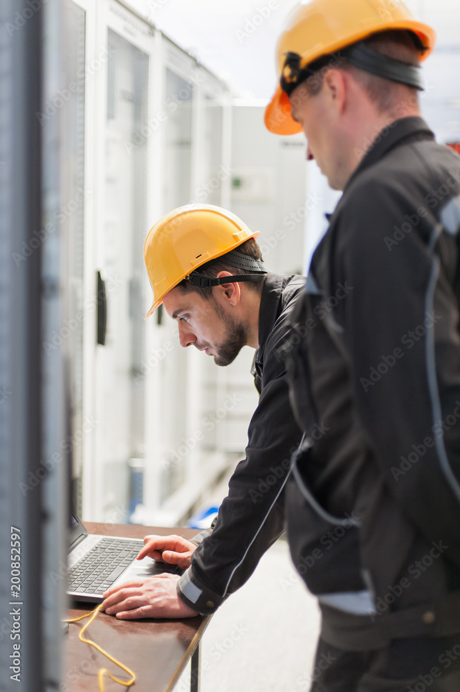 Wall mural field service engineers inspect relay protection system with laptop computer