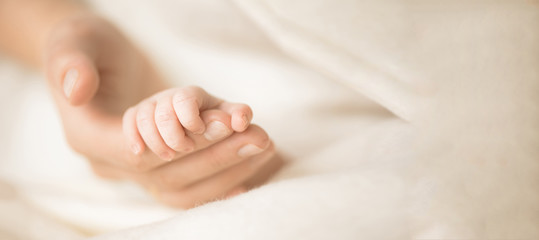 Female hand holding her newborn baby's hand. Mom with her child. Maternity, family, birth concept. Copy space for your text. Banner - Powered by Adobe