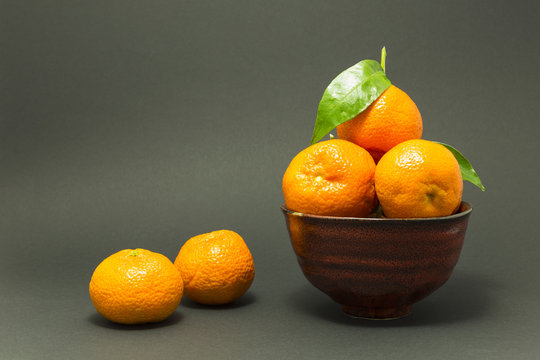 Still life studio shot of a red ceramic bowl with black texture filled with fresh orange tangerines on gray background.