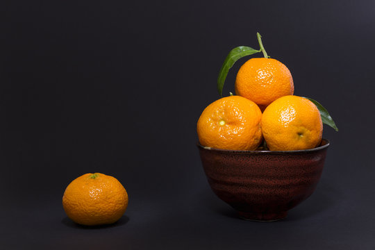 Still life studio shot of a red ceramic bowl with black texture filled with fresh orange tangerines on gray background.