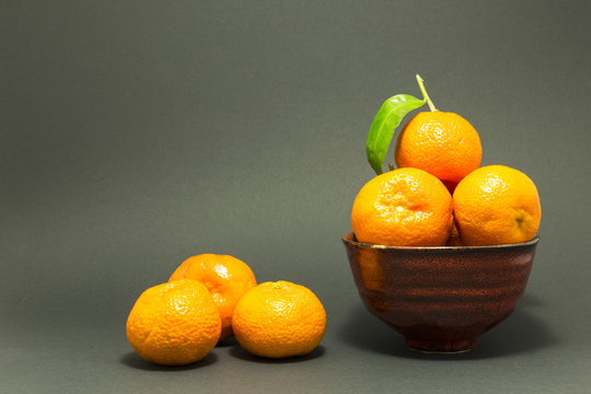 Still life studio shot of a red ceramic bowl with black texture filled with fresh orange tangerines on gray background.