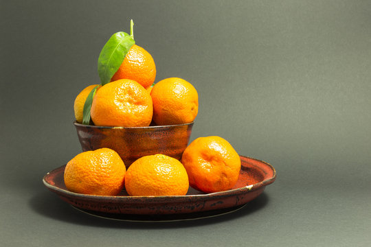 Still life studio shot of a red ceramic bowl and plate with black texture filled with fresh orange tangerines on gray background.