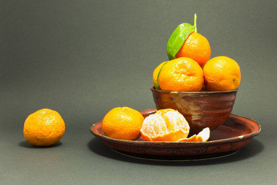 Still life studio shot of a red ceramic bowl and plate with black texture filled with fresh orange tangerines on gray background.