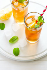 Glasses of iced tea with lemon slices and mint on white wooden background