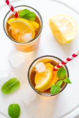 Glasses of iced tea with lemon slices and mint on white wooden background
