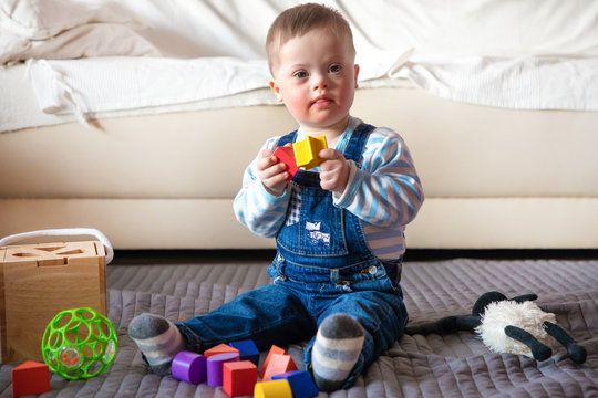 Portrait of cute baby boy with Down syndrome playing in home living room