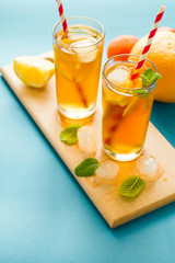 Glasses of iced tea with lemon slices and mint on turquoise wooden background