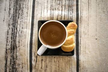 Greek (or Turkish) coffee in a white cup accompanied by a bun