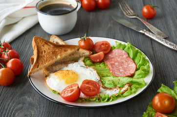 Fried egg, tomatoes, sausage, slices of bread and lettuce on a plate     