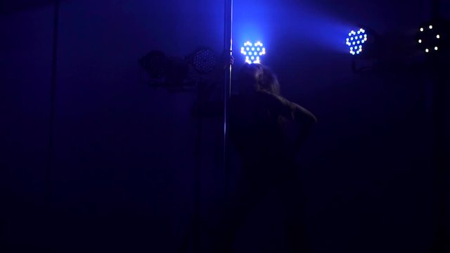 Silhouette of a sexy girl near a pole on a background of bright colored spotlights in a nightclub. Pole dance.
